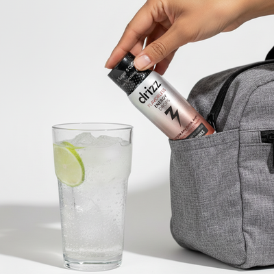 Drizz energy drink bottle being placed into a gray bag next to a glass of ice and lime.