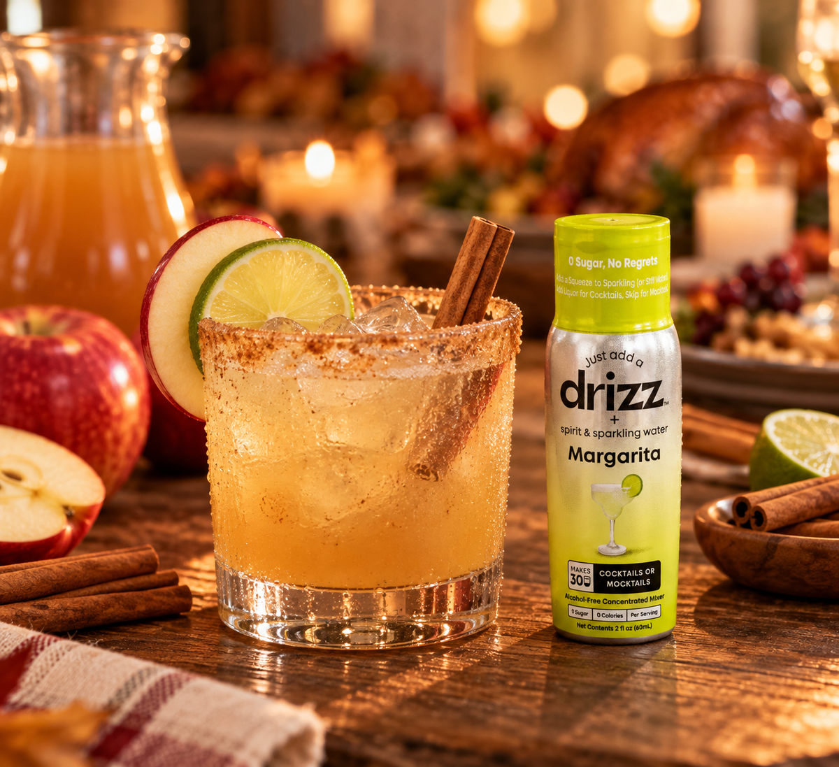 Apple cider margarita mocktail with a cinnamon-sugar rim, apple slice, lime wheel and cinnamon stick next to a bottle of Drizz Margarita Mixer Drops