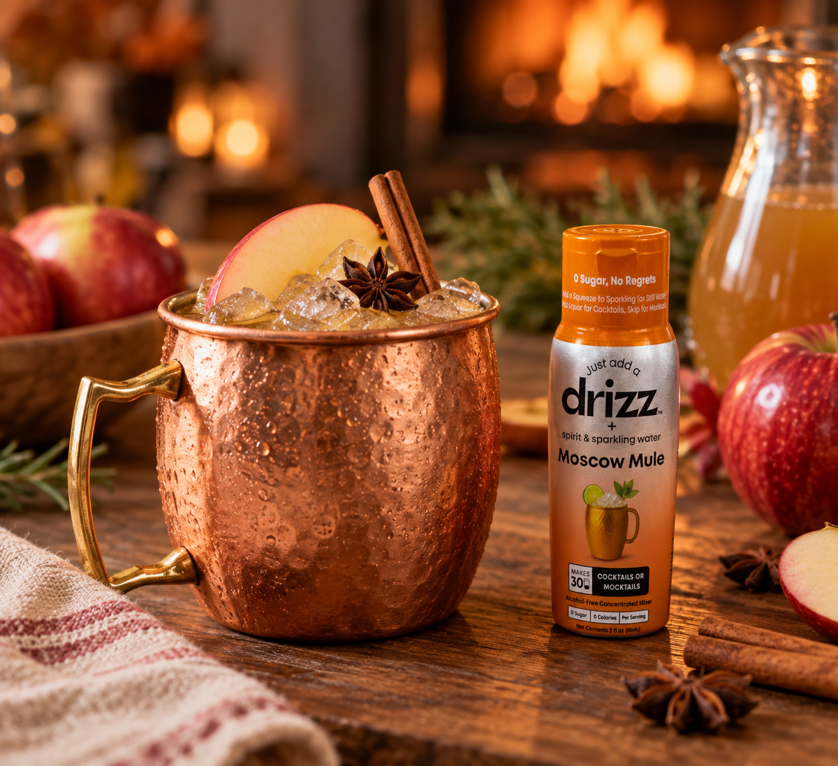 Apple cider mule mocktail in a copper mug with an apple slice, cinnamon stick and star anise next to a bottle of Drizz Moscow Mule Mixer Drops