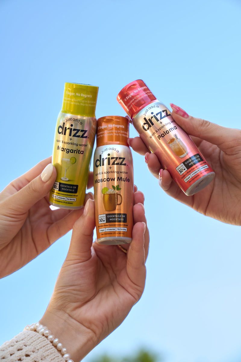 Three Drizz Mixer Drops bottles raised against a blue sky