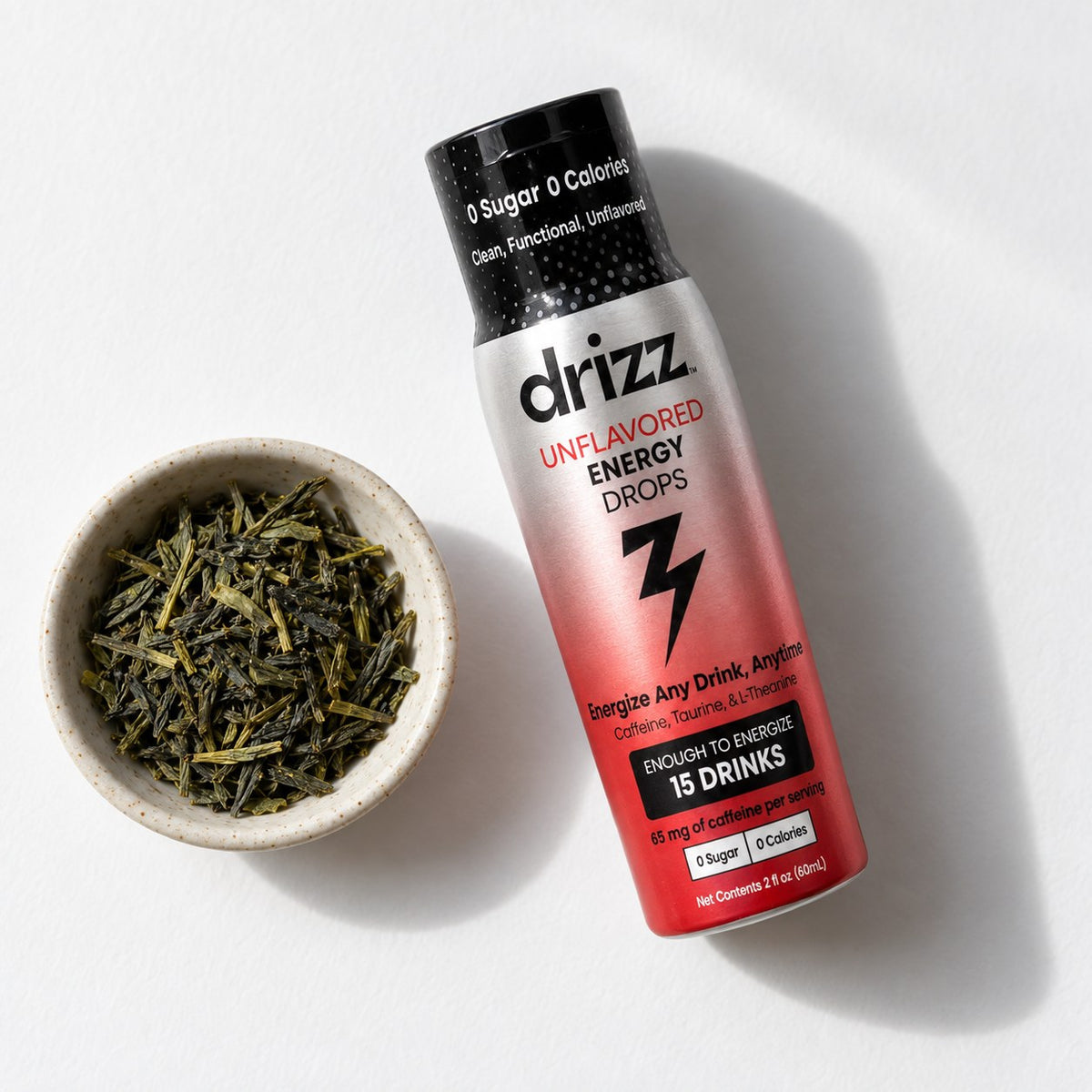 Loose green tea leaves in a bowl beside a bottle of Drizz Unflavored Energy Drops