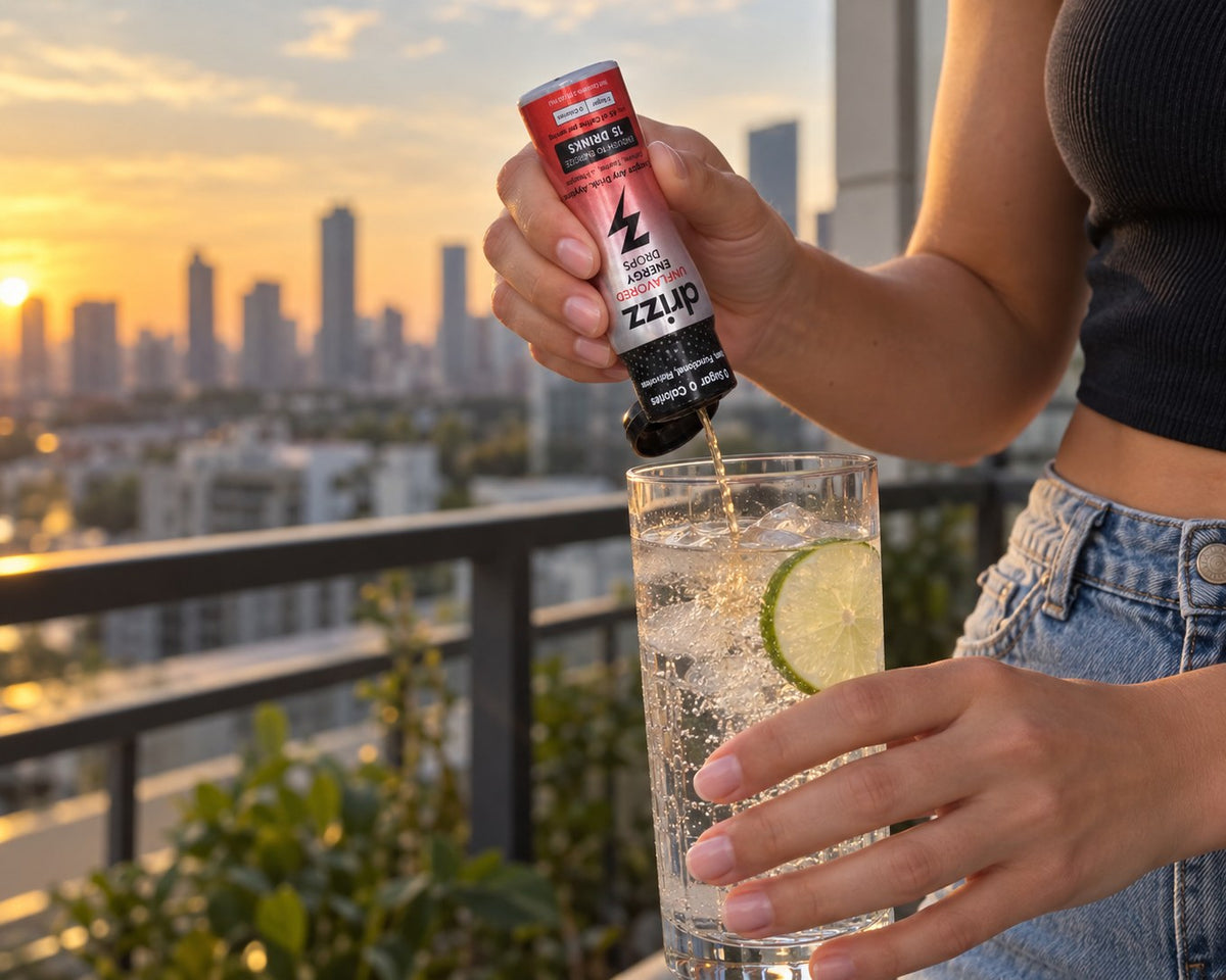 Hands squeezing Drizz Unflavored Energy Drops into a glass of sparkling water on a balcony at sunset