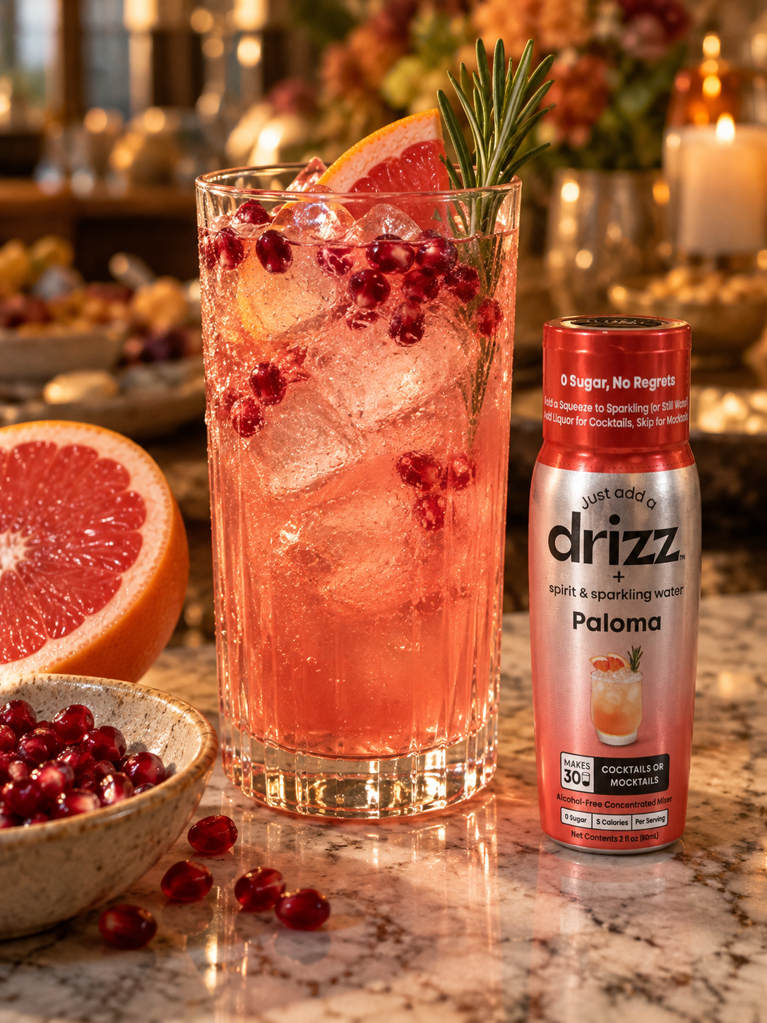 Pomegranate paloma mocktail with grapefruit, pomegranate seeds and rosemary next to a bottle of Drizz Paloma Mixer Drops